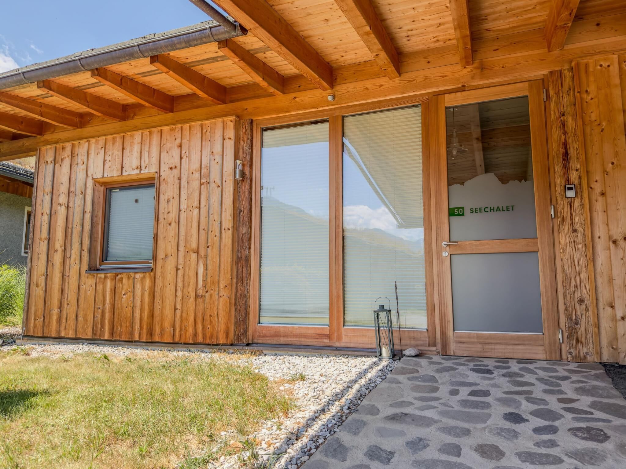 A wooden cabin with a stone-paved entrance, large sliding glass doors, and a visible number '50' on the door.