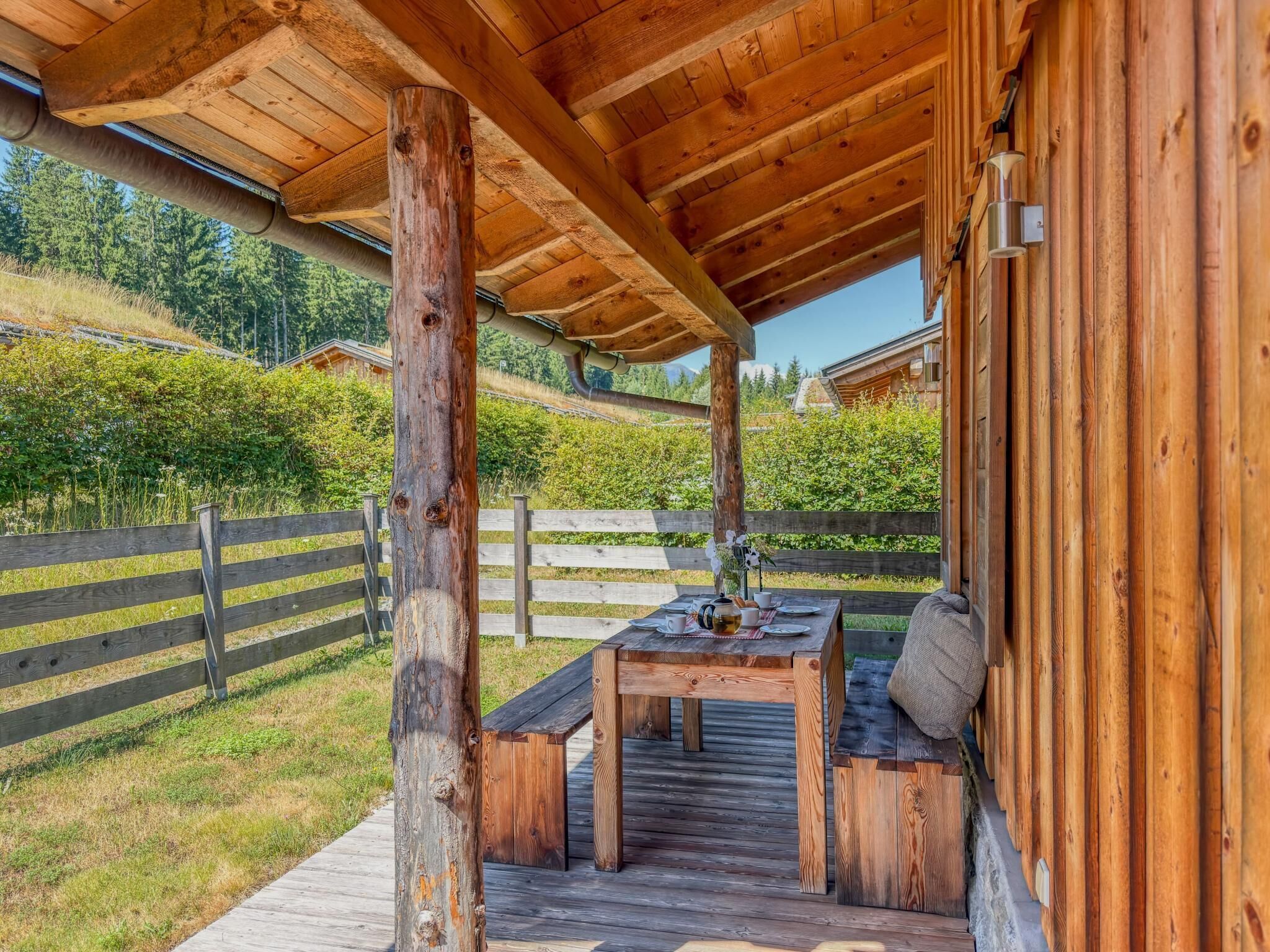 Eine Holzterrasse mit Tisch und Bänken, umgeben von einem Holzzaun und viel Grün.