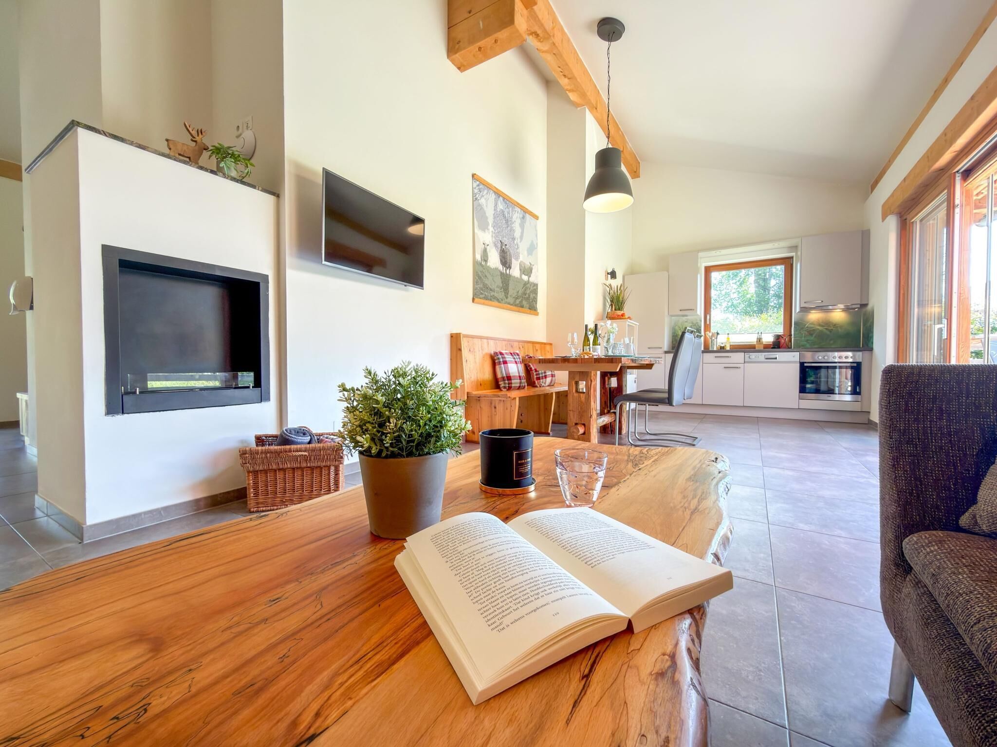 A modern living room with a wooden coffee table, a book, a potted plant, and a television.
