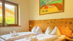 Un lit bien fait, avec du linge de lit blanc et des serviettes soigneusement disposées, une tête de lit en bois, une fenêtre donnant sur un paysage verdoyant et un tableau accroché au mur.