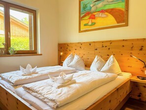A neatly made bed with white linens and towels arranged on it, a wooden headboard, a window with a view of greenery, and a painting on the wall. - Chalet with sauna near Nassfeld-Pressegger See (Hermagor-Pressegger See)