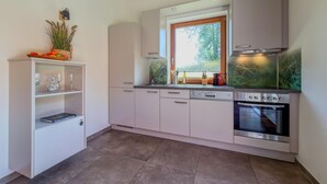 Une cuisine moderne avec des armoires blanches, un four encastré et une fenêtre donnant sur un paysage verdoyant.