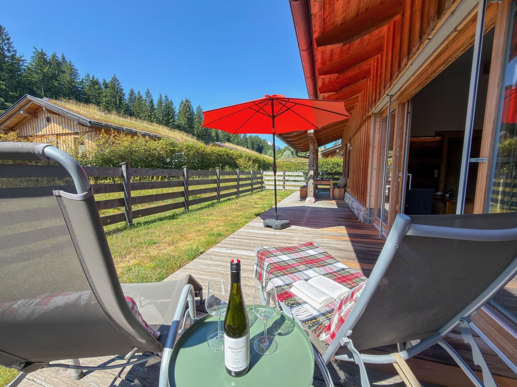 A patio with a table, chairs, a wine bottle, and an umbrella.
