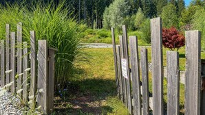 Une clôture en bois avec une pancarte, entourée de verdure et d’arbres.