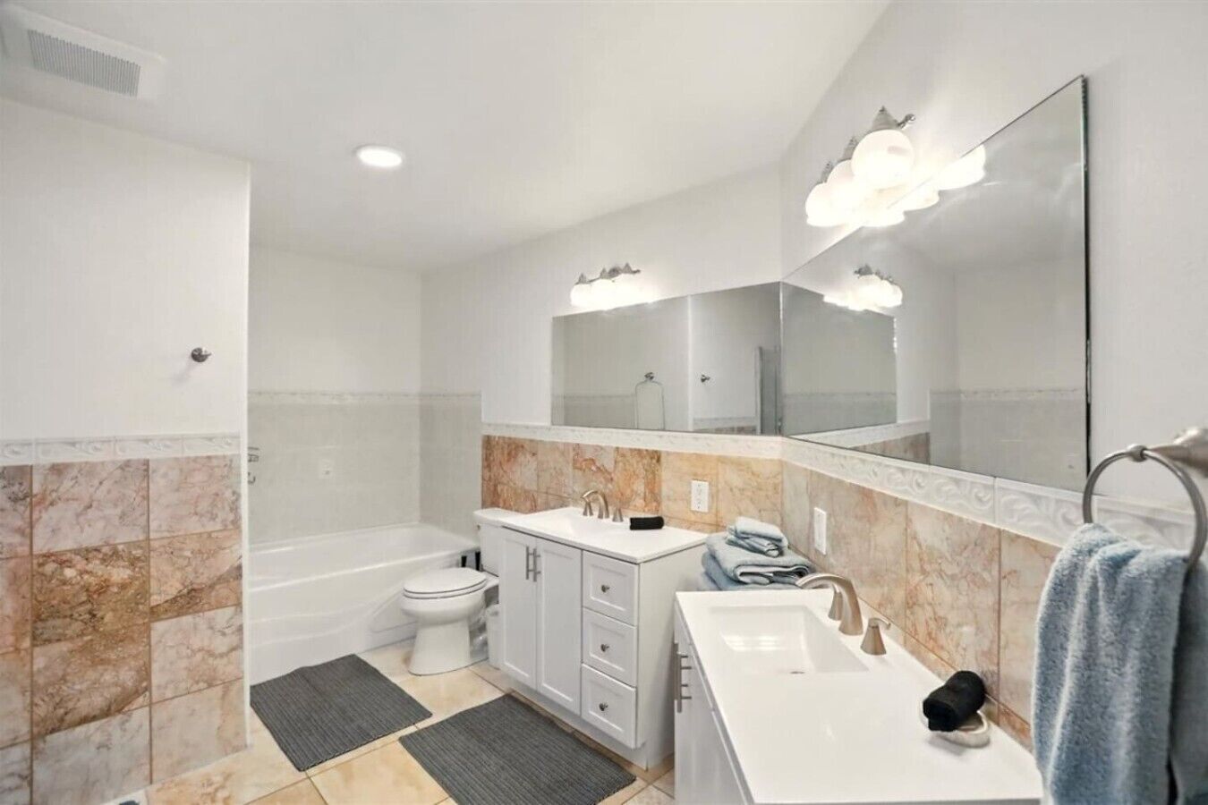 A modern bathroom with a bathtub, toilet, vanity, and large mirror.