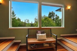 Ein Zimmer mit einer Sitzbank, zwei Fenstern und Blick auf Bäume.