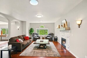 Ein geräumiges Wohnzimmer mit Kamin, einer Couch, zwei Sesseln und einem Couchtisch.
