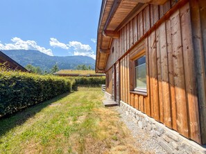 Un bâtiment en bois, avec des fondations en pierre, un ciel dégagé et une chaîne de montagnes en arrière-plan.