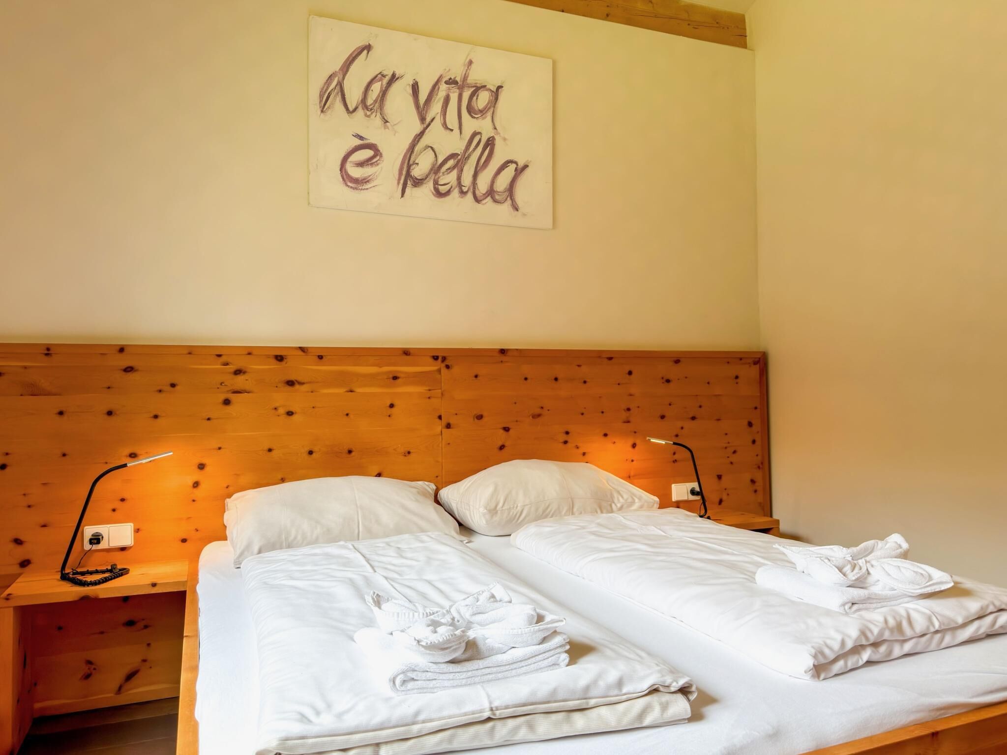 Un lit double avec du linge de lit blanc, deux lampes de chevet et une tête de lit en bois.