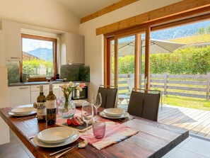 Ein Essbereich mit einem Tisch für zwei, eine Küche im Hintergrund und ein Gartenblick durch große Fenster.