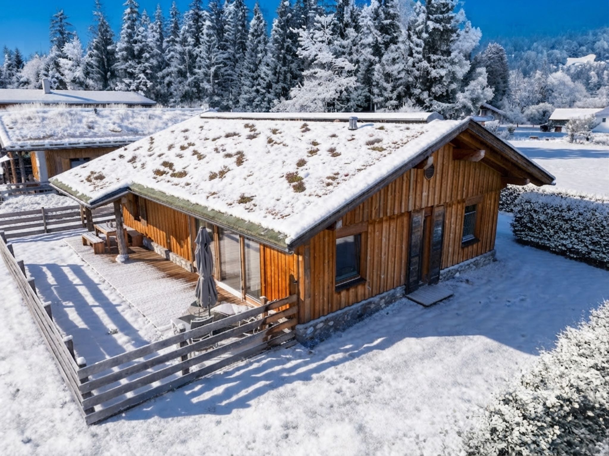 A wooden cabin with a snow-covered roof, a porch with a bench, and a clear view of the surrounding snowy landscape.