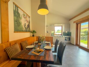 A dining area with a wooden table set for four, a painting on the wall, and a kitchen in the background. - Chalet with sauna and garden near Pressegger See (Hermagor-Pressegger See)