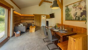 Una habitación amplia con techo de madera, un comedor con mesa dispuesta para cuatro personas, y una zona de estar acogedora con sofá y sillones.