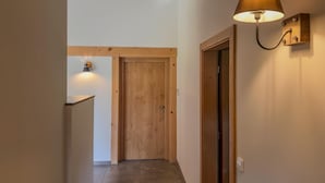 Un pasillo con una puerta de madera al final, una lámpara de pared y un estante peque ño.