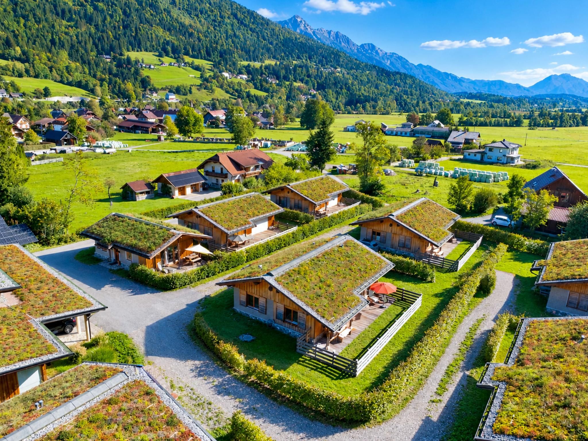 A village with traditional houses featuring green roofs, surrounded by lush greenery and mountains.