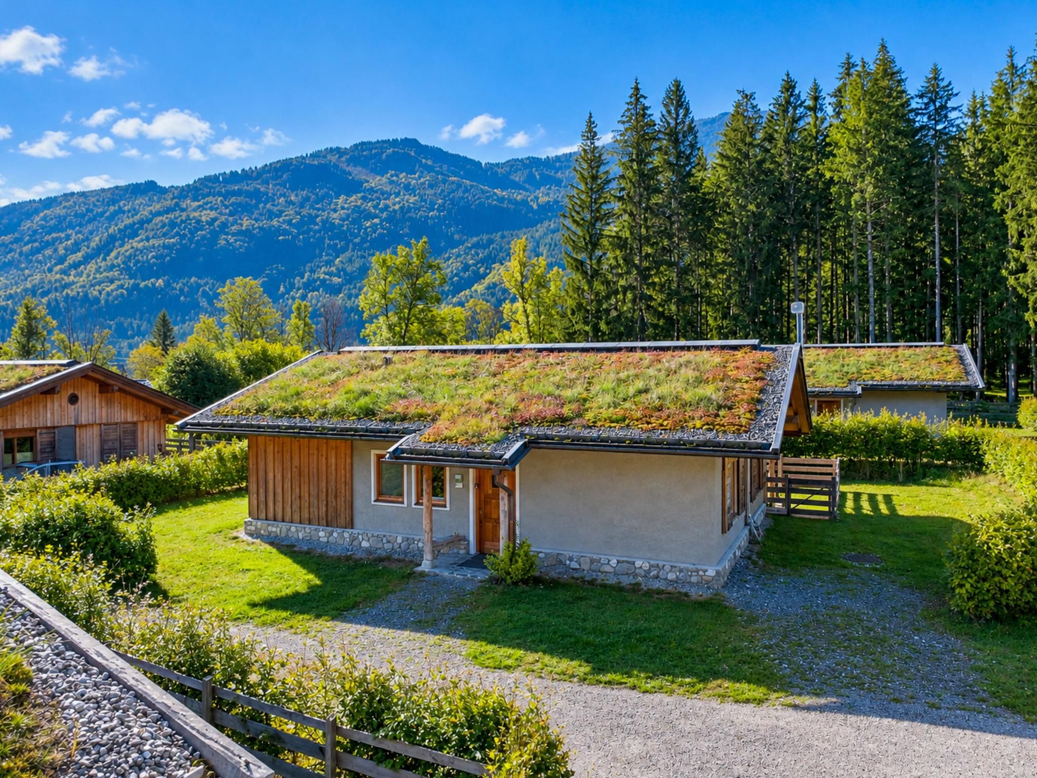 Une maison moderne et écologique, dotée d’un toit végétalisé, entourée d’un jardin bien entretenu et offrant une vue sur les montagnes.