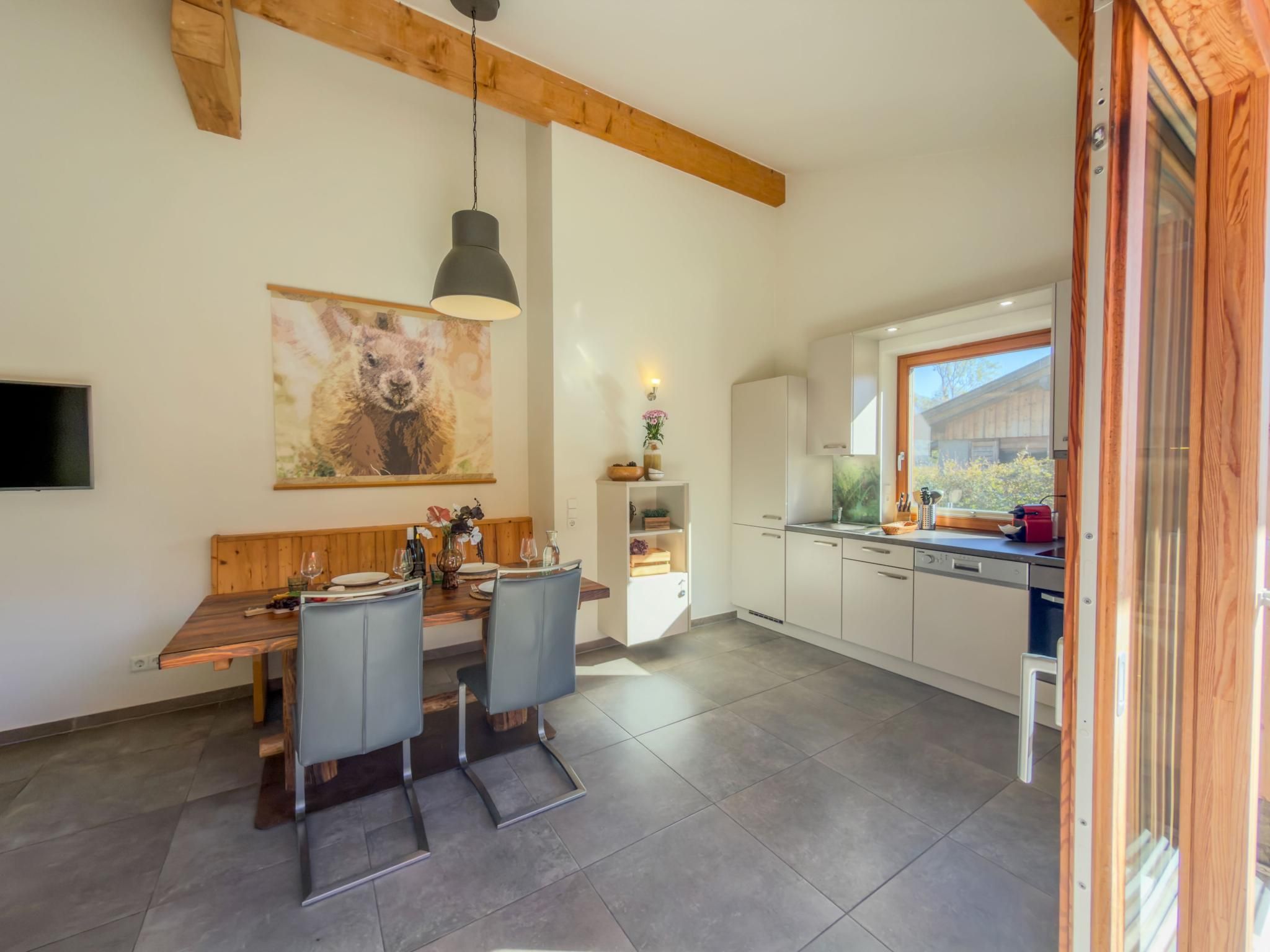 A modern kitchen with white cabinets, a wooden dining table, and a large window.