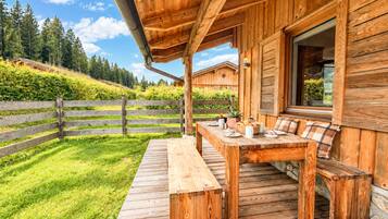 Eine Holzterrasse mit Tisch und Bänken, umgeben von einem Holenzaun und üppigem Grün.
