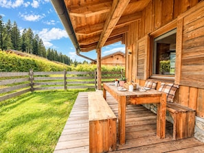 A wooden deck with a table and benches, surrounded by a wooden fence and lush greenery.