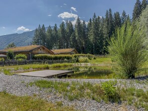 Un chalet rustique doté d’une terrasse en bois et situé près d’un étang, dans une zone boisée.