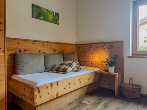 Una cama de madera con cabecera, almohadas, una mesita de noche con una planta y una ventana.