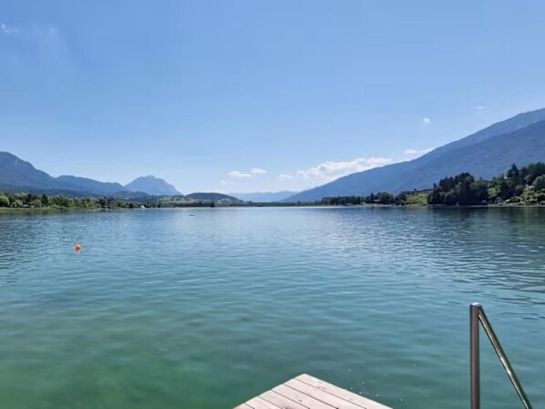 A calm lake with mountains in the background, a wooden dock, and a clear sky.