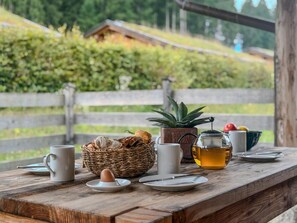A wooden table with a basket of bread, a teapot, a cup, and a plate with an egg.