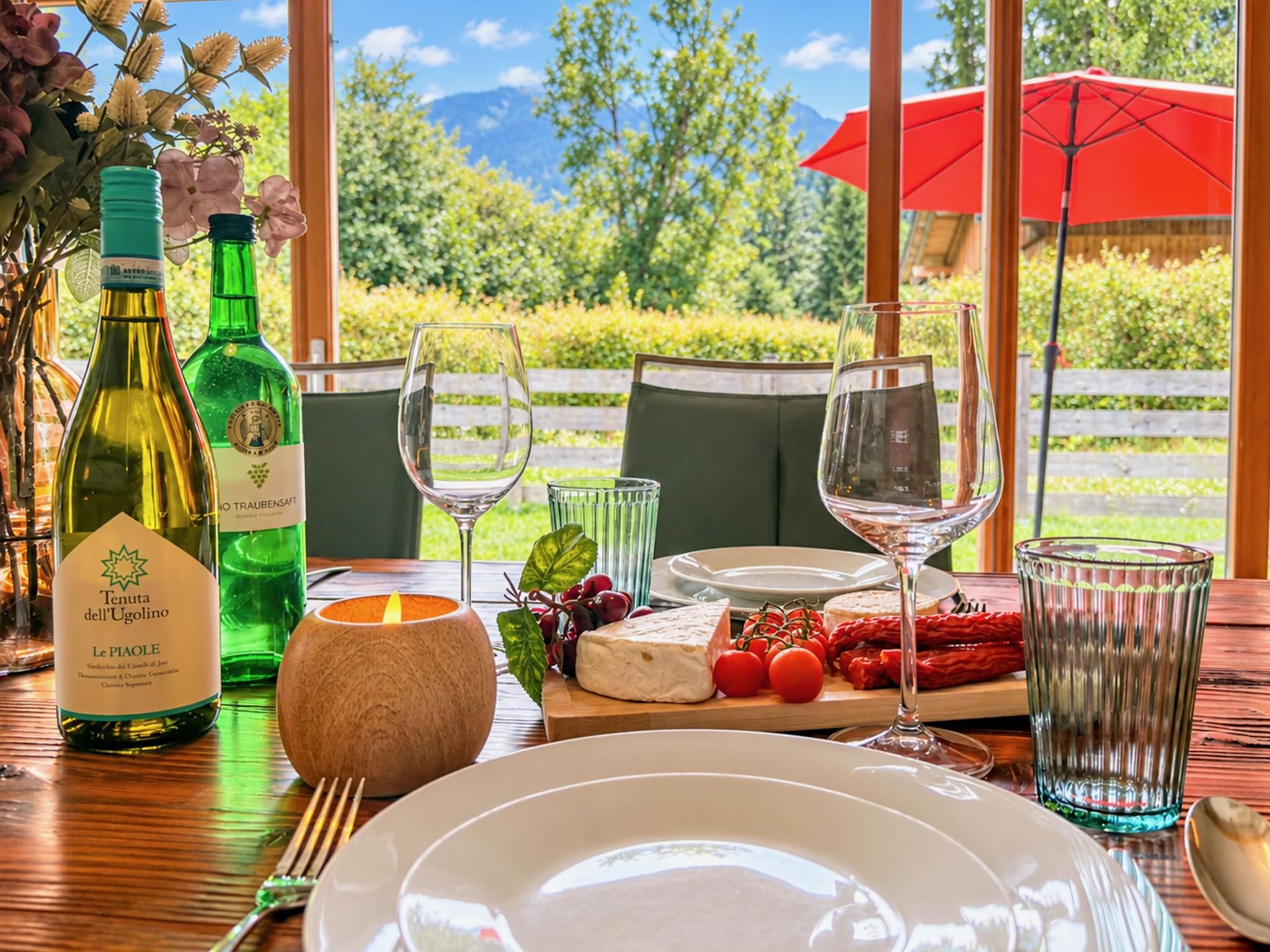Ein gedeckter Tisch mit Speisen, Weinflaschen, Gläsern, einer Kerze und einer Käseplatte mit Tomaten und Paprika.