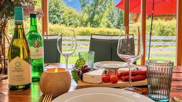 Ein gedeckter Tisch mit Speisen, Weinflaschen, Gläsern, einer Kerze und einer Käseplatte mit Tomaten und Paprika.