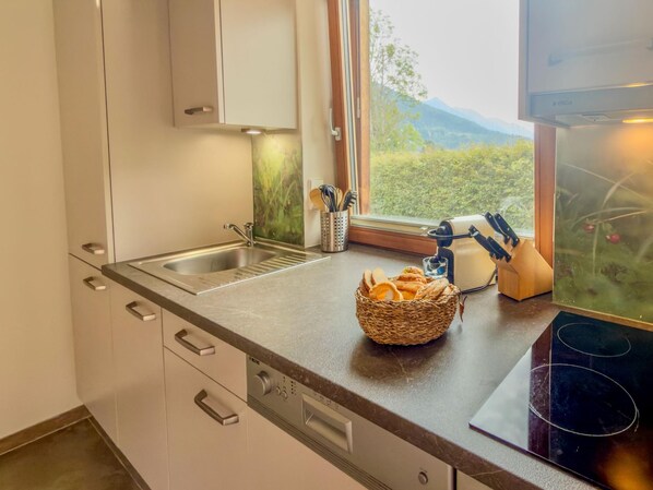 Una cocina con un lavamanos de acero inoxidable, una ventana con vistas a la vegetación y una cesta de pan sobre la encimera.