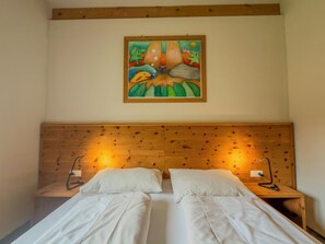 A room with a wooden headboard, two white beds, and a colorful painting above the bed.