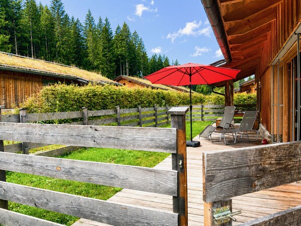 Une terrasse en bois avec un parasol rouge, des chaises longues et une vue sur une zone boisée.