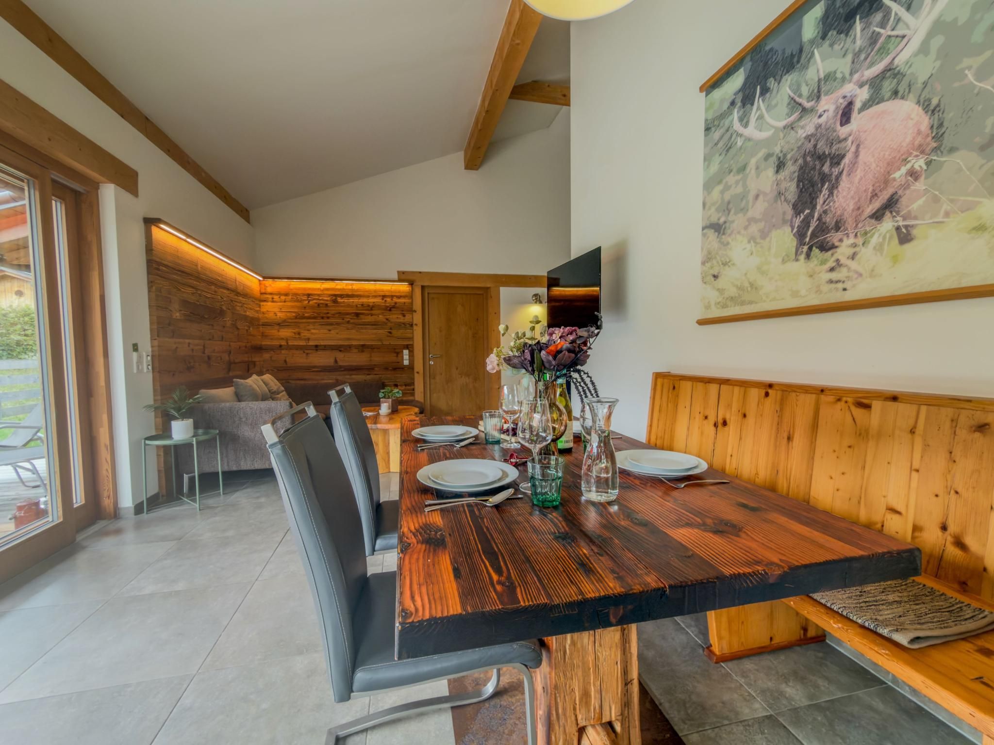 A dining area with a wooden table set for four, a bench along the wall, and a large painting of a deer.
