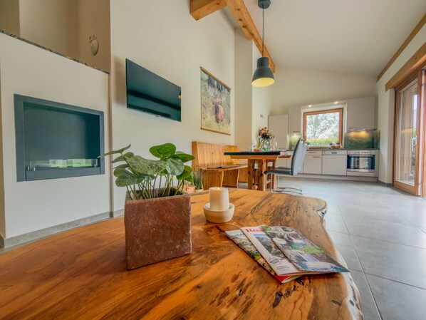 A modern kitchen with a wooden table, a potted plant, and a magazine.