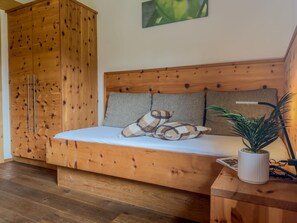 Un lit en bois avec une tête de lit, deux oreillers, une table de chevet avec une plante et une armoire en bois.