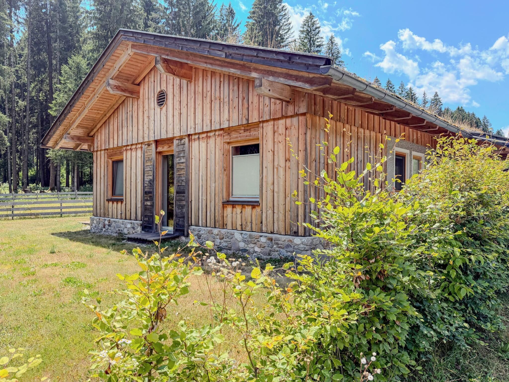 Eine Holzhütte mit steinernen Fundamenten, großen Fenstern und einem geneigten Dach.