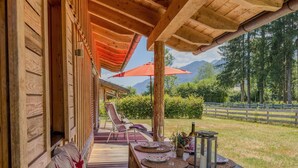Eine Holzterrasse mit überdachter Sitzecke, einem Tisch mit Kerze und Glas, und Blick auf eine gebirgige Landschaft.