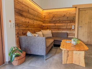 Una habitación de esquina con una pared de madera, un sofá gris con cojines, una mesita de madera y una cesta de mimbre con una planta.