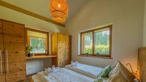 Ein Schlafzimmer mit einem Bett, einem Holzschrank und einem Fenster mit Blick auf Grünfläche.