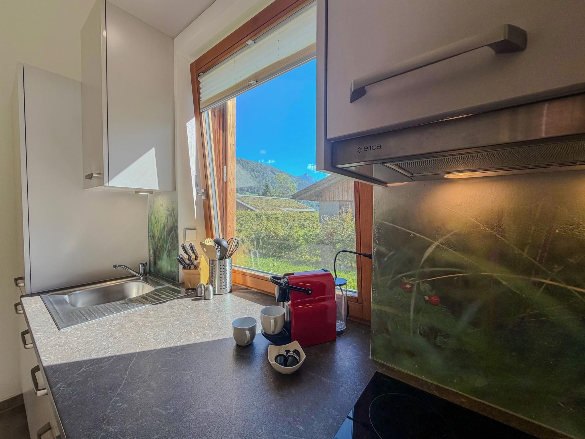A kitchen with a window, a sink, a red kettle, and a coffee maker.