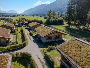 A rural village with traditional wooden houses, a gravel path, and a mountainous backdrop.