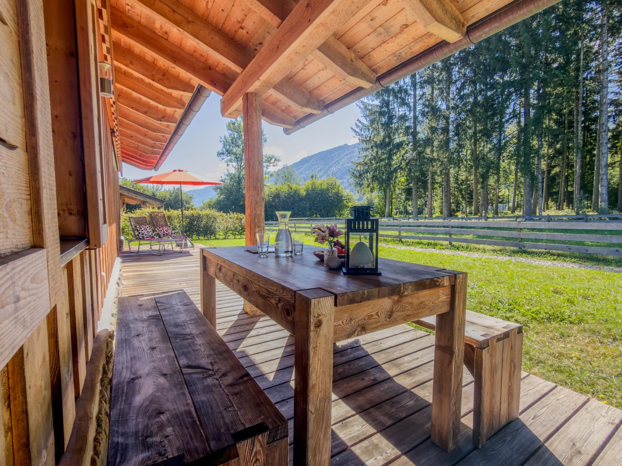 A wooden deck with a table and benches, overlooking a forested area with a mountain in the distance.