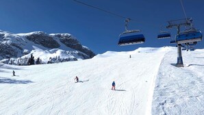 Een skipiste met skiërs, een stoeltjeslift en besneeuwde bergen.