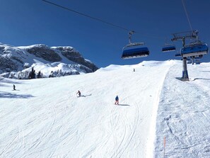 Eine Skipiste mit Skifahrern, einem Sessellift und schneebedeckten Bergen.