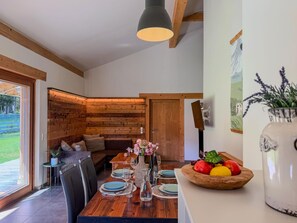 A dining area with a wooden table set for two, a vase with flowers, and a bowl of fruit.