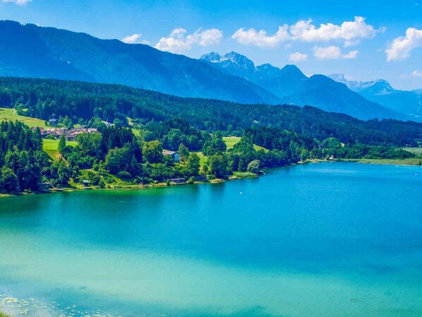 Ein See, umgeben von Bergen und viel Grün, mit einer kleinen Siedlung am Ufer.