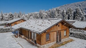 Een houten chalet met een sneeuwbedekte dak, omringd door met sneeuw beladen bomen en een heldere lucht.
