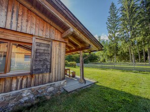 A wooden cabin with a stone foundation, a wooden deck, and a view of a forest. - Chalet with sauna near the Nassfeld region (Hermagor-Pressegger See)