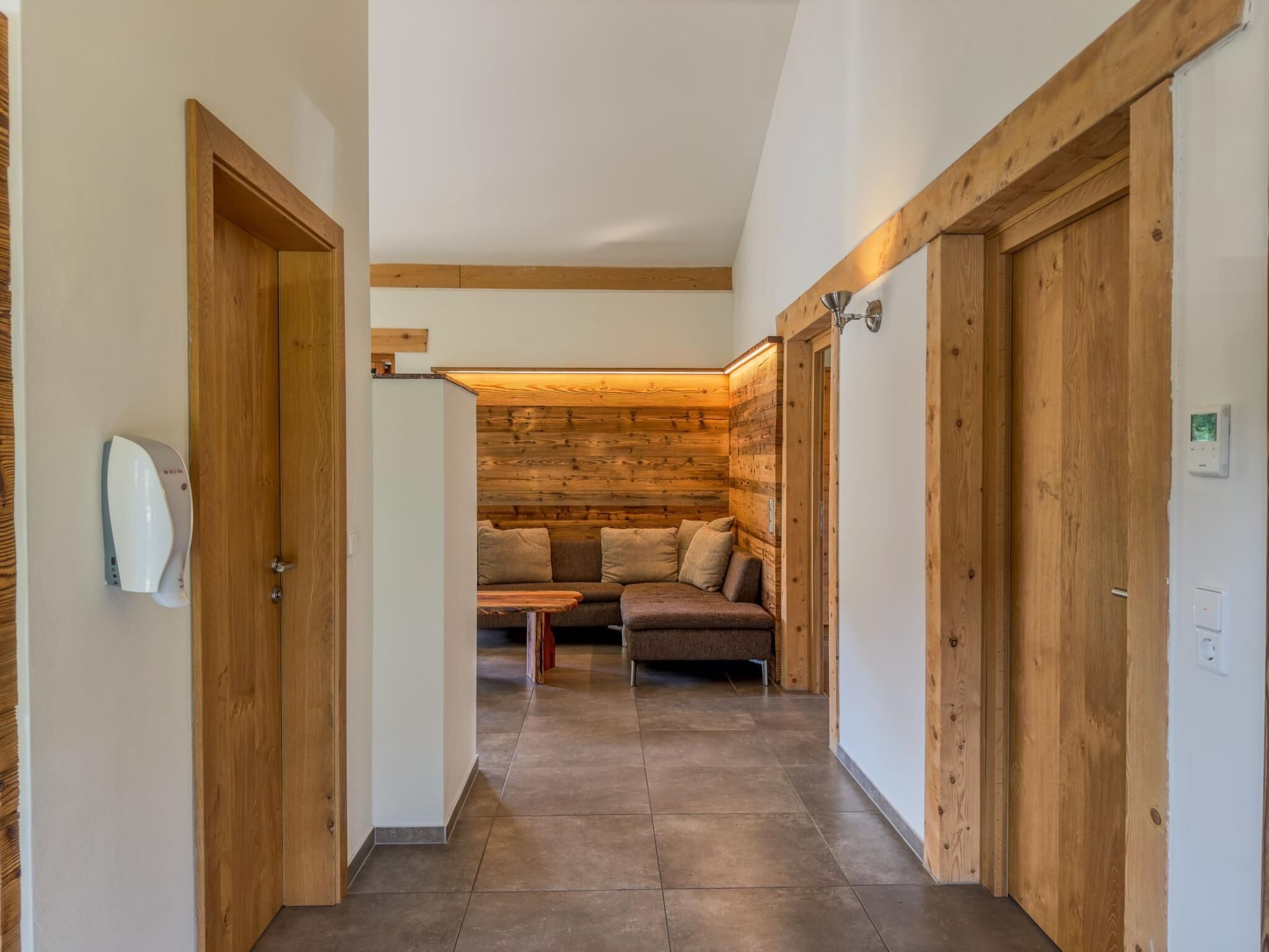 A hallway with wooden walls and doors, leading to a seating area with a sofa and a table.