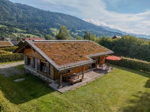 Ein Holzhaus mit geneigtem Dach und einem begrünten Dachgarten, umgeben von einem gepflegten Rasen und Blick auf Berge.